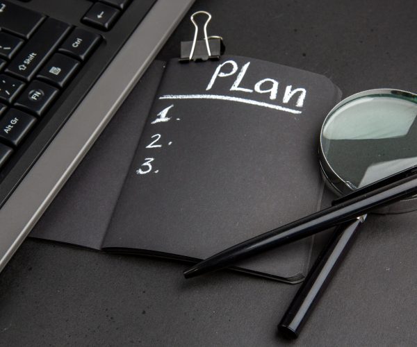 bottom-view-plan-written-black-notepad-lupa-keyboard-binder-clip-pen-black-background